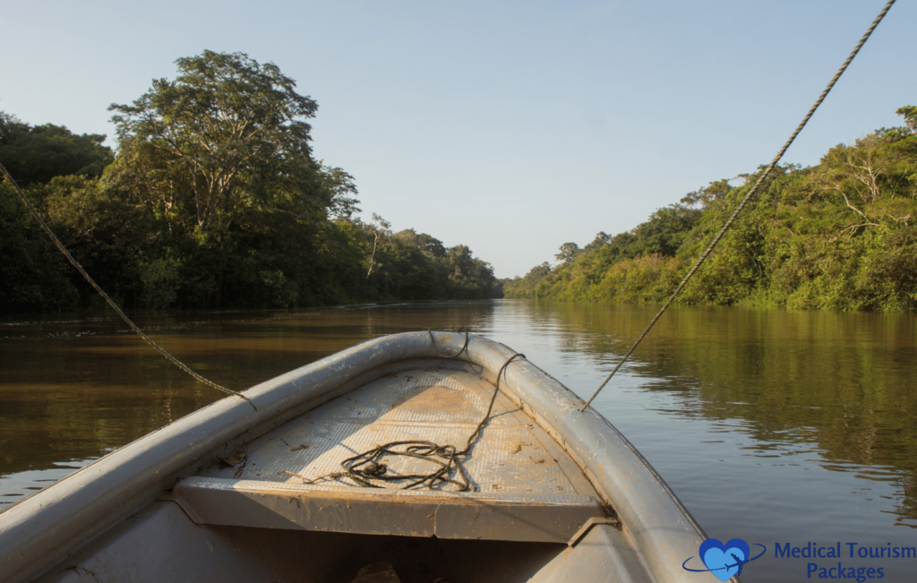 A boat glides along a calm river, embraced by Colombia's dense green trees under a clear blue sky, making it one of the country's premier tourist attractions.