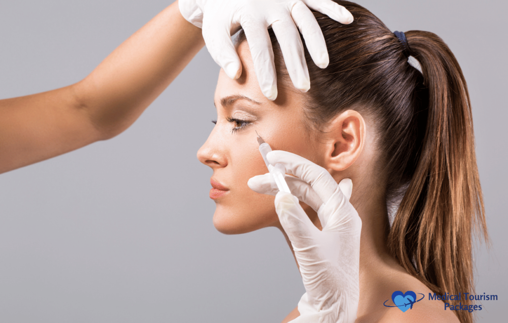 A person receives a Botox procedure in the side of their face, assisted by two gloved hands against a plain background.