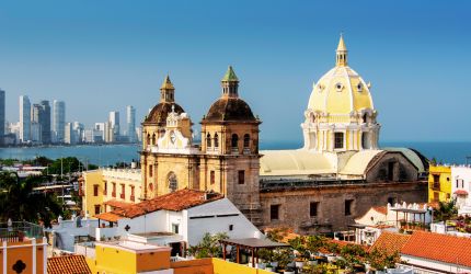 Historic cathedral with yellow dome and two towers stands against a city skyline and blue ocean in Cartagena, Colombia—a perfect spot to unwind and rejuvenate in the heart of Caribbean Renewal.