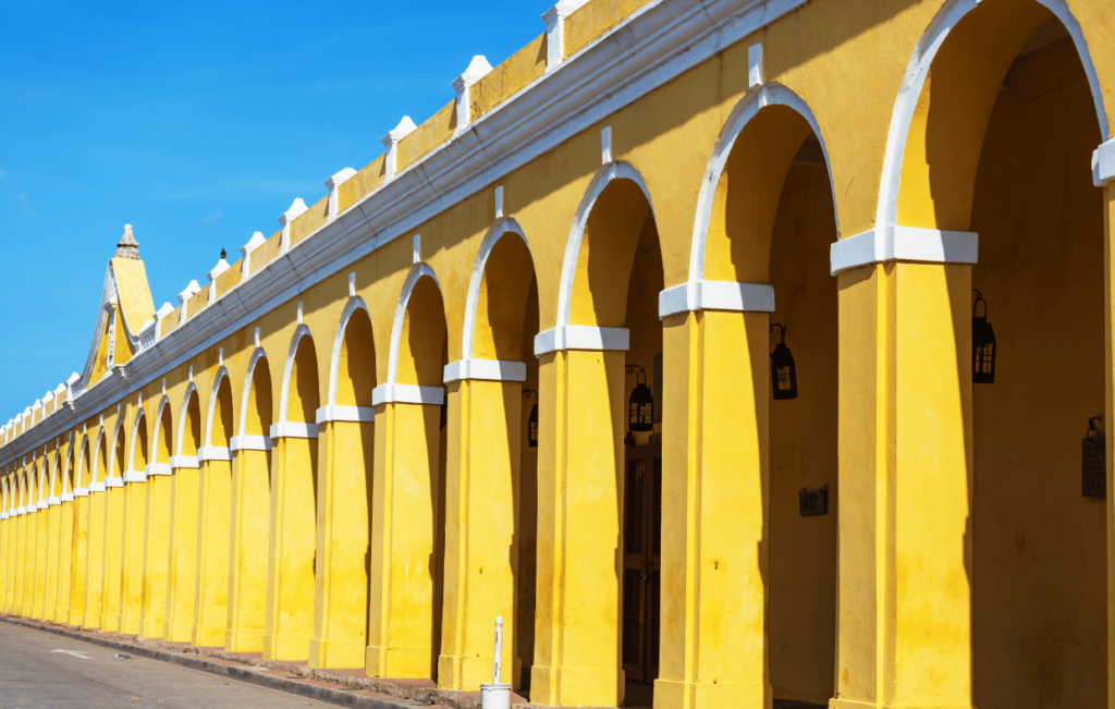 A long yellow building with white archways stands gracefully under the clear blue sky, reminiscent of Cartagena's vibrant charm.