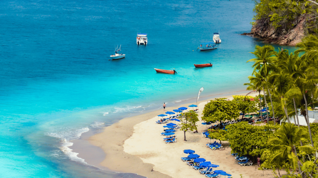 A tropical beach in Costa Rica with turquoise water, several boats anchored offshore, and a row of blue beach chairs under umbrellas lining the sandy shore offers the perfect relaxation spot for American medical tourists seeking a tranquil respite.