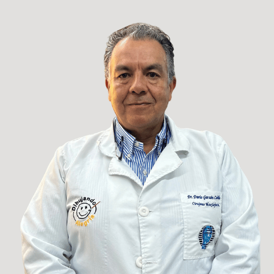 Dr Dario wearing a white coat with embroidery stands against a plain background.