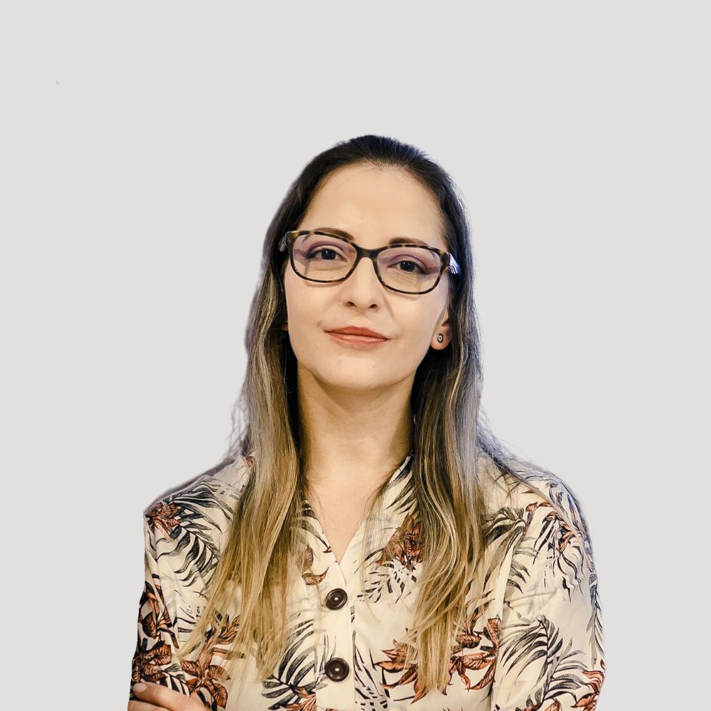 Dr. Patricia, with her long hair and glasses, stands confidently in a floral patterned blouse against a plain light background.