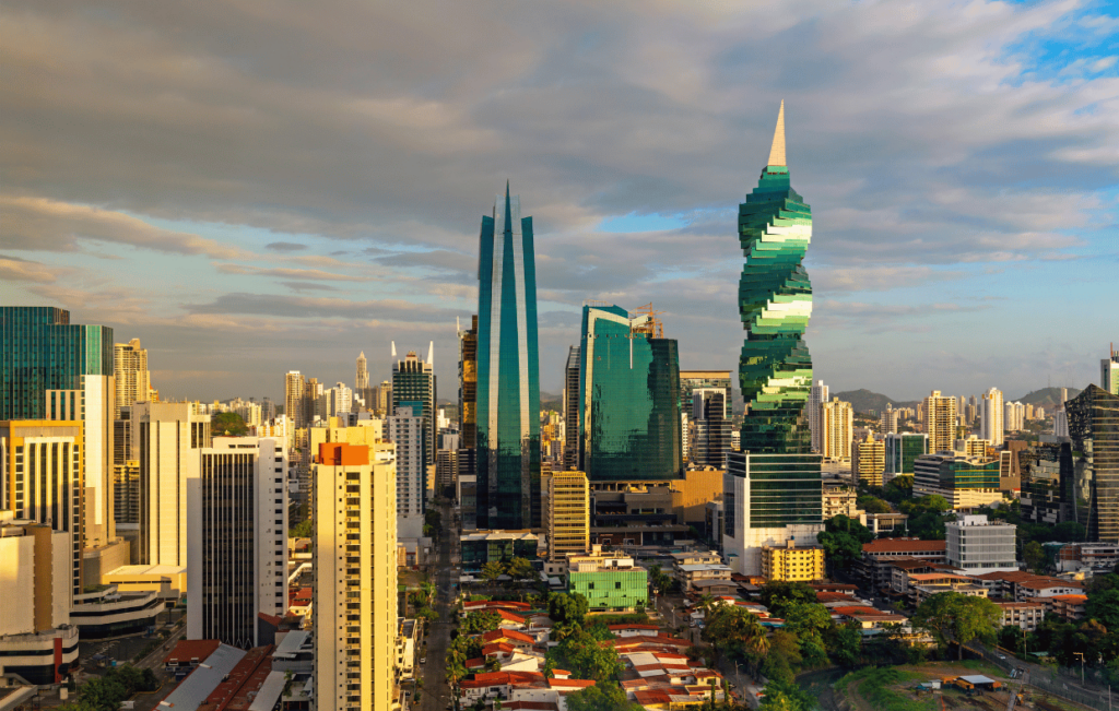 Moderno horizonte de la ciudad de Panamá al atardecer, con sus característicos rascacielos de cristal verde, incluida la emblemática Torre F&F, con los barrios tradicionales visibles más abajo, mostrando la mezcla de arquitectura contemporánea y desarrollo urbano de la ciudad.