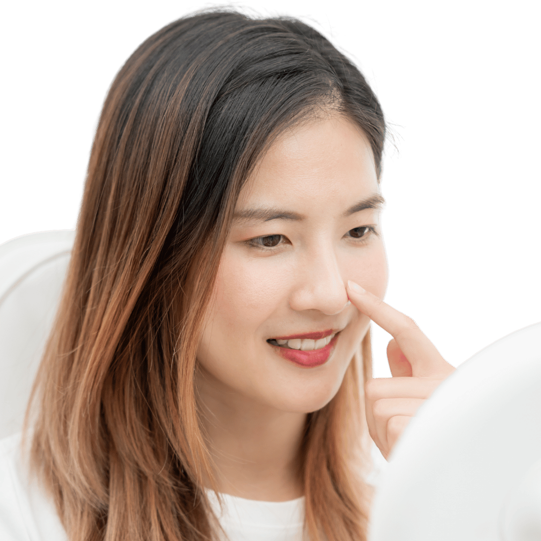 A woman smiling and touching her nose while looking at a mirror.