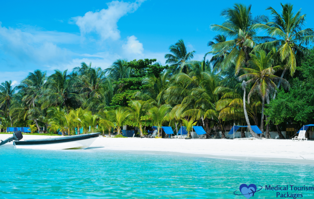 A serene tropical beach in Colombia boasts clear turquoise waters, palm trees, and blue lounge chairs under the sun. A white boat is anchored near the shore, making it a must-see spot in every travel guide to top tourist attractions.