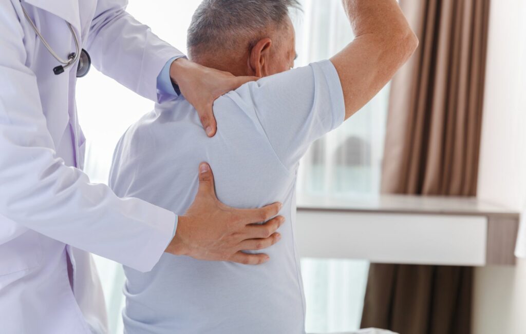 In a bright room, a doctor, specializing in orthopedic surgery, assists a man in stretching his arm during a physical examination.