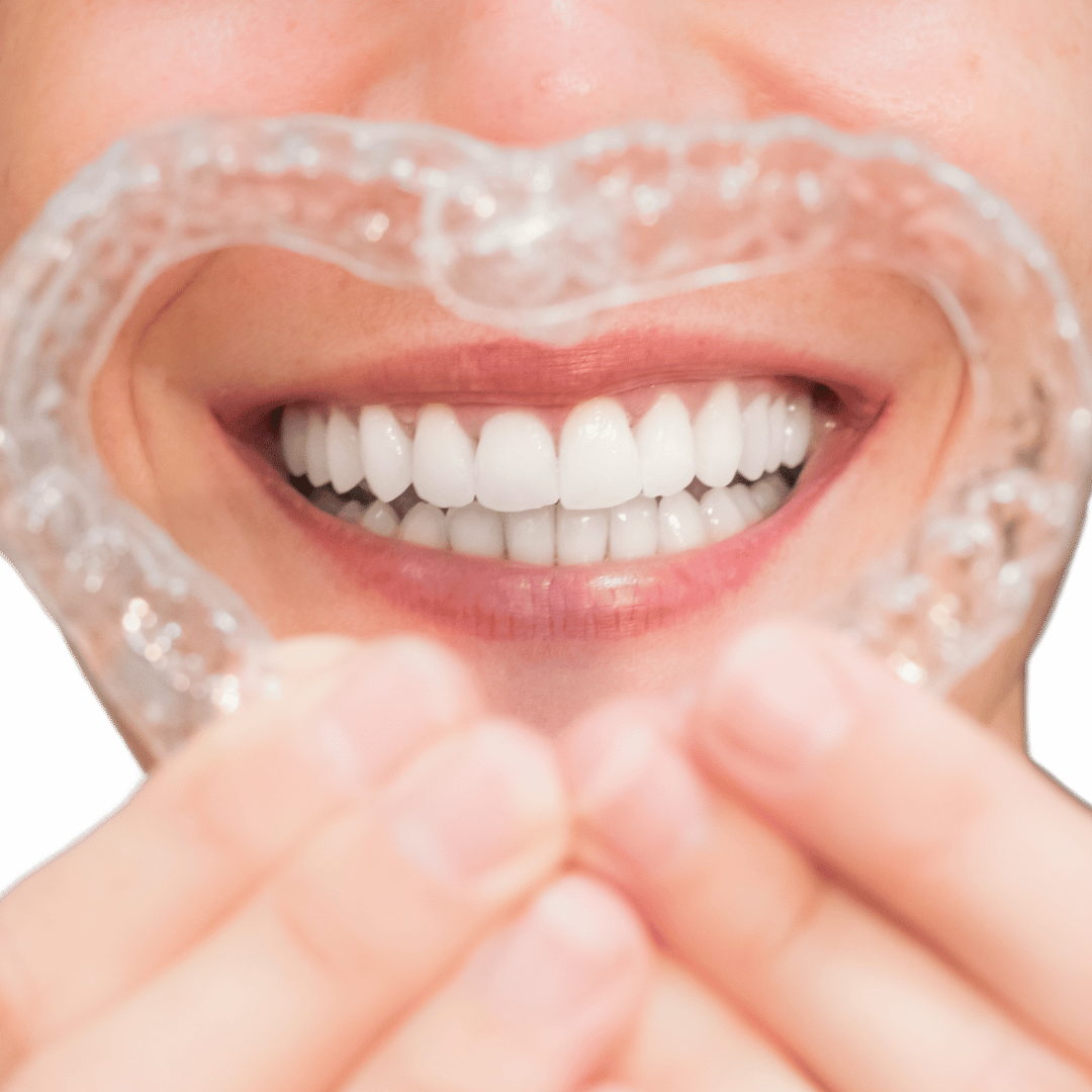 Person smiling and holding a clear dental retainer in front of their teeth.