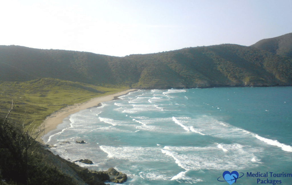 Aerial view of a scenic Colombian beach with gentle waves and surrounding green hills under a clear sky, perfect for those seeking top tourist attractions.